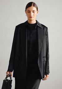 Čierny oversize blazer s mierne textúrovaným povrchom, so zárezovým golierom, prednými vreckami a prispôsobeným strihom.