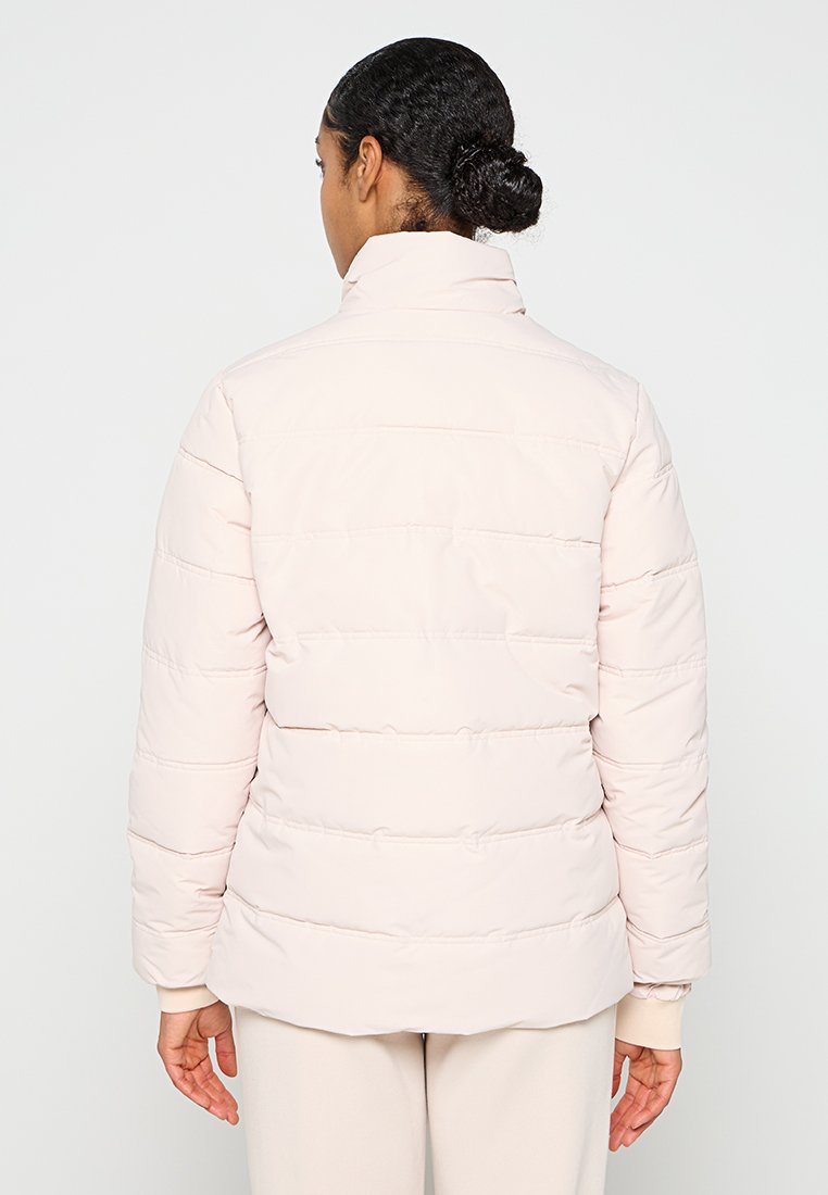 Lichtroze pufferjack met een horizontaal doorgestikt patroon, hoge kraag en elastische manchetten. Glad textuur, middellange lengte, aansluitende silhouet.