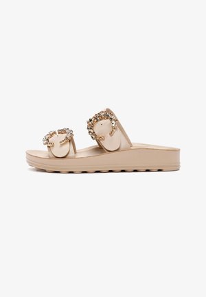 Sandale plateforme beige à glissière avec deux brides ornées de grosses boucles décoratives en bijoux et semelle à adhérence texturée.