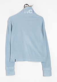 Giacca in pile azzurro chiaro con collo alto, caratterizzata da un logo sottile sul colletto e polsini strutturati. Tessuto morbido, vestibilità comoda.