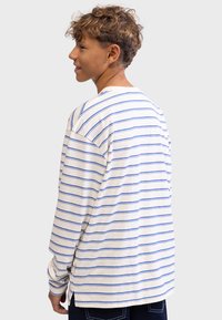Long-sleeve striped shirt in cream with blue horizontal lines, featuring a relaxed fit and side slits at the hem. Soft cotton material.