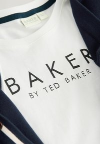 Witte T-shirt met "BAKER BY TED BAKER" in vet zwart lettertype. Heeft een marineblauwe kraag en is gemaakt van katoen.