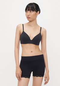 Zwarte beha met een diepe V-halslijn en dunne bandjes, gecombineerd met zwarte shorts met een kanten zoom. Beide kledingstukken hebben een gladde textuur.