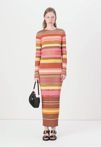 Abito a maniche lunghe a coste con righe orizzontali nei colori rosa, arancione, marrone e giallo. Indossato con una borsa nera e sandali.