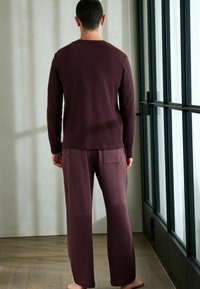 Dunkelrotes Langarmhemd und Nadelstreifenhose, beide aus weichem Stoff. Das Hemd hat einen runden Ausschnitt, die Hose verfügt über eine Gesäßtasche und eine lockere Passform.