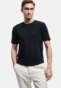 Black short-sleeve t-shirt with a crew neckline, made of ribbed fabric. Paired with light-colored, loose-fitting trousers.