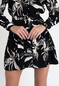 Abito nero con motivo floreale bianco e grigio, dotato di vita accentuata da una cintura, maniche lunghe e bottoni decorativi sui polsini. Tessuto testurizzato con plissettature.