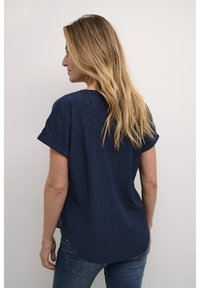 Haut bleu marine à manches courtes avec un design texturé comportant des découpes en diamant et un ourlet arrondi, associé à un jean bleu.