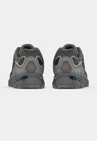 Ζευγάρι αθλητικών παπουτσιών σε σκούρο γκρι και μαύρο χρώμα με το λογότυπο GEL, εμφανιζόμενο από πίσω σε λευκό φόντο.