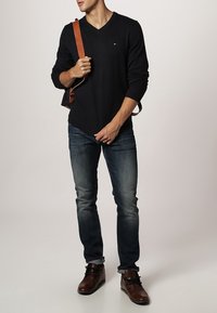 Pull à col en V noir, jean slim bleu, bottines marron, et sac à bandoulière marron. Tissu robuste et design décontracté.