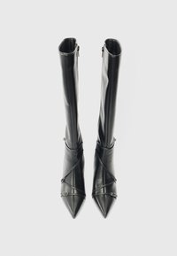 Botas de cuero negras hasta la rodilla con punta afilada, que cuentan con cierres de cremallera y un diseño de correas entrecruzadas con acentos de hardware metálico.