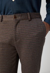 Brown and blue checkered trousers with a textured surface, featuring a button closure and side pockets. The waistband is neatly finished.