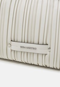 Witte leren plissé tas met zilveren Kar Lagerfeld-logoplaatje en nageldetails aan de voorkant onderaan.