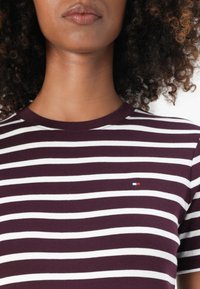 Bordeaux en witte gestreepte t-shirt met een ronde hals. Voorzien van een klein logo op de borst. Zachte, aansluitende stof, minimalistisch ontwerp.
