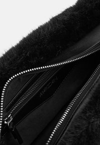 Schwarze Handtasche mit einer weichen, fellartigen Textur oben und einem glatten Lederkörper. Verfügt über einen silbernen Reißverschluss und mehrere Innenfächer.