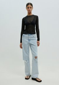 Schwarzes langärmeliges Mesh-Top, hellblaue, ausgewaschene, weit geschnittene Jeans und schwarze Flip-Flops. Auffällige Risse und ein leicht gewaschenes Denim-Design.
