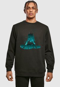 Felpa nera con una grafica turchese di un cappello da strega con la silhouette di un castello, su uno sfondo testurizzato.
