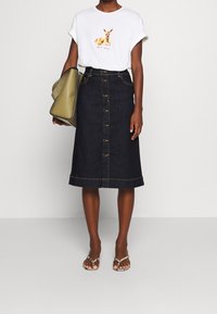 Tmavě modrá denimová midi sukně s předními knoflíky, s kontrastním lemem. V kombinaci s bílým tričkem s grafikou a zelenou kabelkou. Sandály dokončují vzhled.