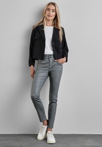 Svart cropped jacka, vit t-shirt, grå tajta byxor och vita sneakers. Jackan har ett slagkrage; byxorna har en jämn textur.