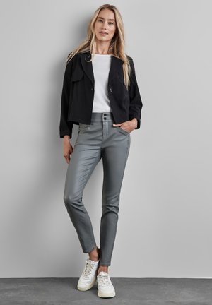 Zwarte cropped jacket, witte t-shirt, grijze slimfit broek en witte sneakers. De jas heeft een reverskraag; de broek heeft een gladde textuur.