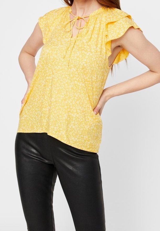 Blusa floreale gialla con maniche corte a volant, dettaglio del collo a cravatta e vestibilità rilassata, abbinata a pantaloni in pelle nera aderenti.