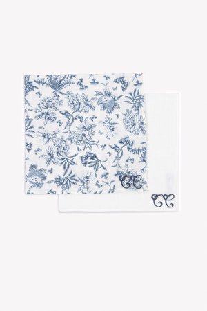 Twee gevouwen katoenen zakdoeken, één wit met blauwe bloemenprint en één effen wit, beide met donkerblauwe geborduurde initialen.