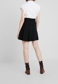 Falda negra acampanada con pliegues, combinada con una blusa blanca de manga corta; acompañada de botas de tacón marrones. Tela suave, diseño hasta la rodilla.