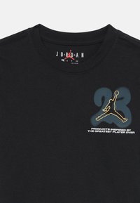 Camiseta negra de Jordan con un pequeño logo dorado de Jumpman sobre un número 23 desgastado y el texto "Productos inspirados por el mejor jugador de todos los tiempos."
