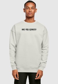 Ljusgrå sweatshirt med texten "ÄR DU RÄDD?" i fet svart stil. Den har en avslappnad passform och ribbat avslut vid ärmar och nederkant.