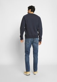 Sweatshirt en coton bleu marine avec col ras du cou, poignets et ourlet côtelés, associé à un jean en denim bleu. Coupe décontractée, design sobre, sans motifs ni embellissements visibles.