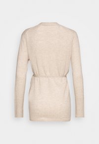 Beige långärmad stickad tröja med mjuk textur, bälte i midjan och en enkel rund hals. Sömmar synliga på axlar och ärmar.