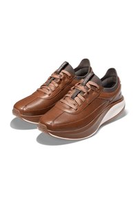 Sneakers in pelle marrone con un design perforato, punta arrotondata e lacci elastici, dotati di una soletta bianca imbottita e dettagli testurizzati.
