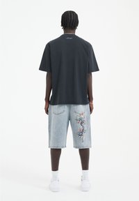 Černé bavlněné tričko, volný střih, s kulatým výstřihem. Světle modré denimové šortky se světlým barevným výšivkou draka na boku. Bílé tenisky.