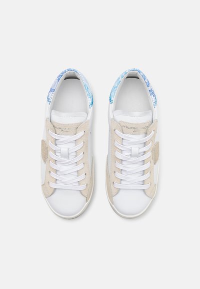 Hvite sneakers med beige semsket skinn detaljer og blå mønstrede fôr. Har klassiske snøringer og en glatt lærtekstur.