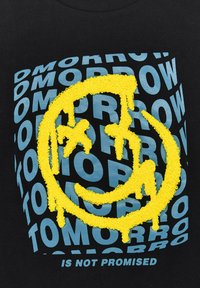 Schwarzes Stoff-T-Shirt mit einem strukturierten gelben Smiley-Gesicht-Graphic. Der Hintergrund zeigt wiederholt blauen Text mit der Aufschrift "MORGEN IST NICHT GARANTIERT."