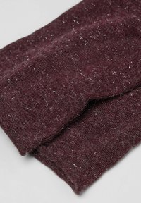 Foldet maroon strikket stof med synligt fnug og pels på en lys grå overflade.