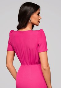 Robe ajustée en tissu rose vif, avec des manches courtes bouffantes et un détail discret de fermeture éclair dans le dos. Texture lisse avec une taille élastique.