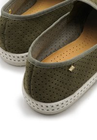 Green suede slip-on shoes with perforated design, a tan insole, and white rubber soles featuring textured accents and a small logo detail.