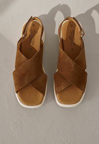 Sandali in suede marrone con cinturini incrociati, punta aperta e suola bianca. Presentano un design con cinturino posteriore e una soletta imbottita.