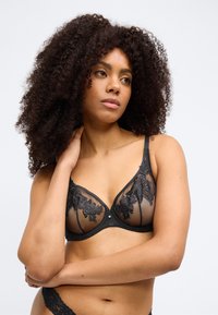 Μαύρο δαντελένιο σουτιέν με διαφανείς επιφάνειες διακοσμημένες με κεντήματα λουλουδιών, με μπανέλα στήριξης, ρυθμιζόμενους ράντες και ελαφρώς κυματιστή λαιμόκοψη.