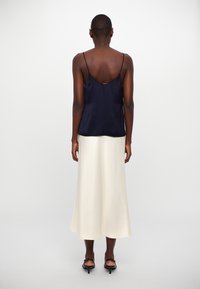 Camisole en satin bleu marine avec des fines bretelles, associé à une jupe en satin crème, dotée d'un ourlet fluide et d'une texture douce et lisse.