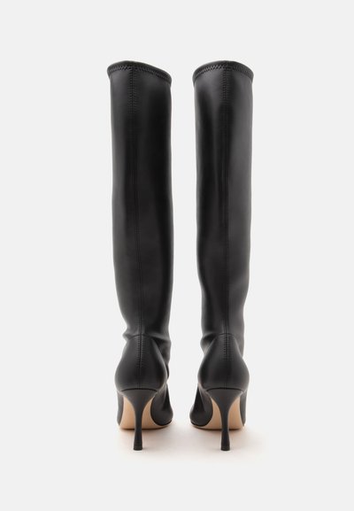 Paire de bottes en cuir noires montantes jusqu'aux genoux avec bouts pointus et talons hauts et fins, vues de dos sur fond blanc.