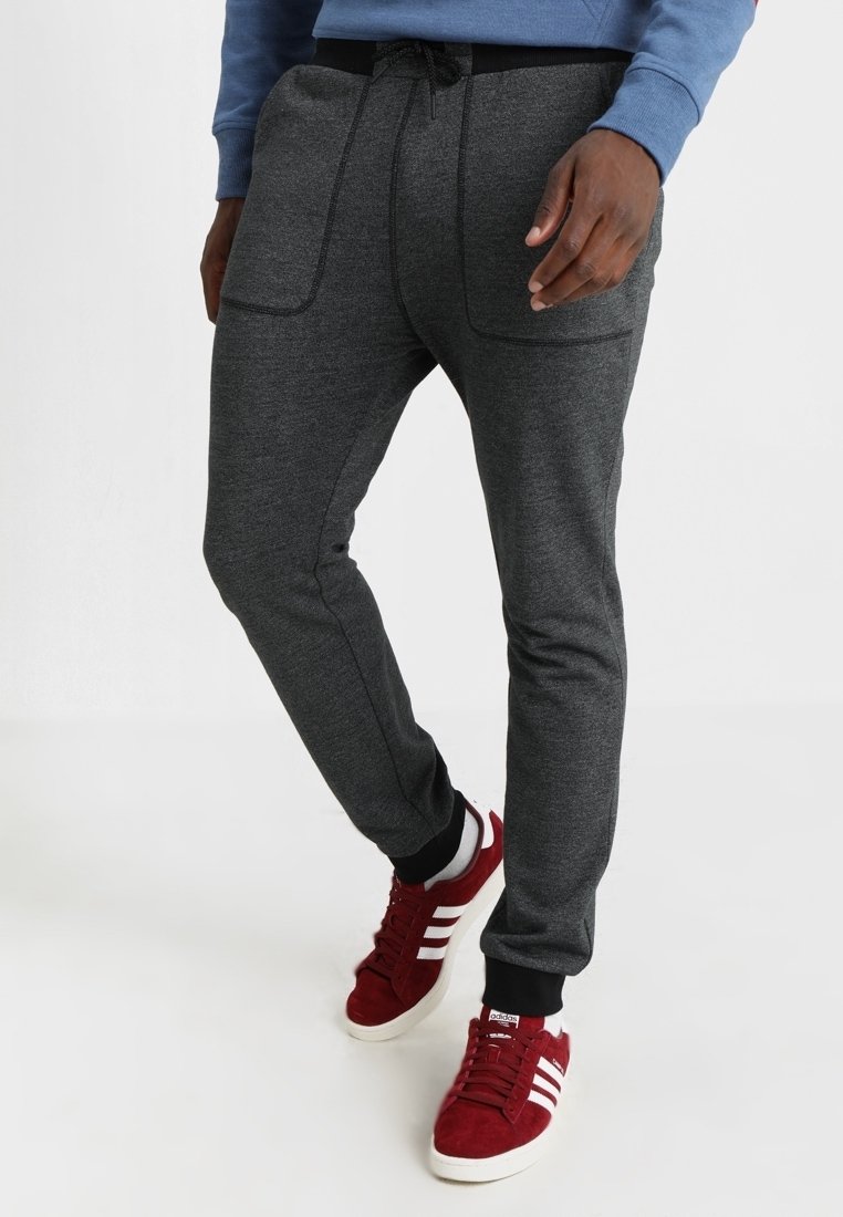 Grå joggerbyxor med elastisk midja och snörning, utrustade med två framfickor och avsmalnande ben, tillsammans med röda sneakers.