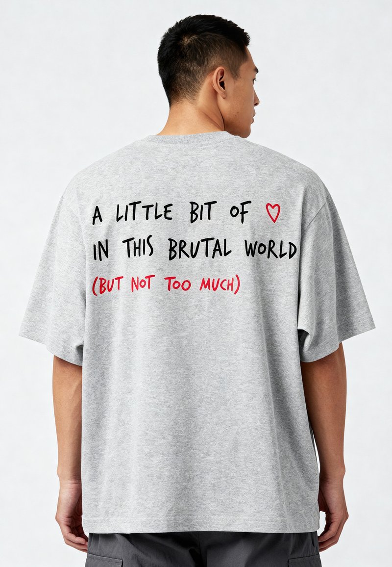 Siva oversized T-shirt z black in rdečim besedilom na hrbtni strani: "MAJHEN KOŠEK ❤️ V TEM BRUTALNEM SVETU (AMPAK NE PREVEČ)."