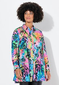 Chemise à boutons colorée avec un design peplum, présentant des motifs audacieux en rose, vert, bleu et noir sur un tissu léger.
