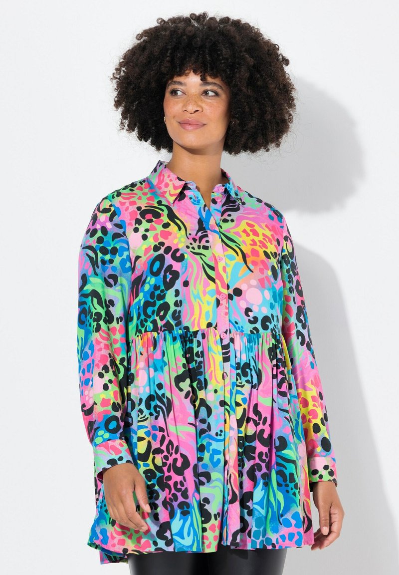 Chemise à boutons colorée avec un design peplum, présentant des motifs audacieux en rose, vert, bleu et noir sur un tissu léger.