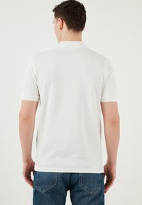 Vit polo med kort ärm, texturerad krage och ribbade manschetter, tillsammans med blå denimjeans. En enkel och ren design.