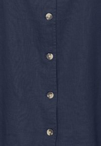 Marineblåt stof med fem lodret justerede, runde, lyse knapper syet på et stykke tøj.