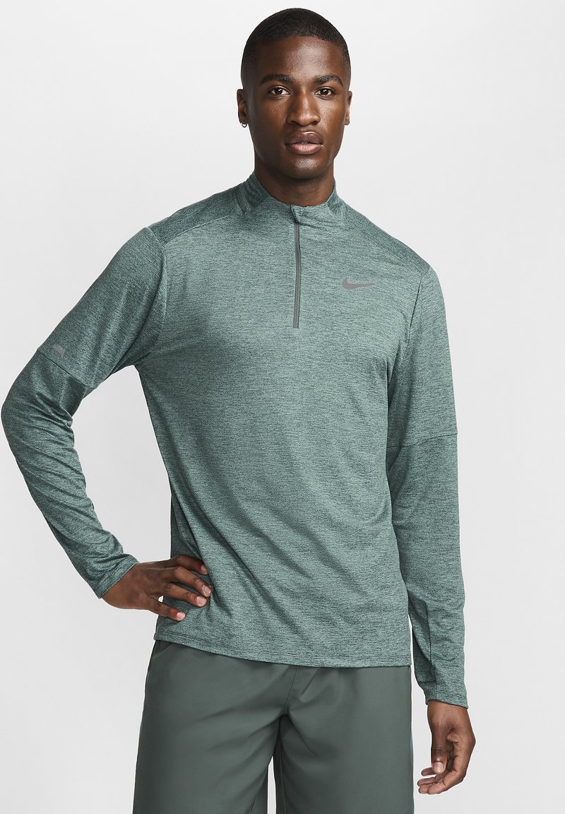 Top verde de manga larga y media cremallera en tejido texturizado con un sutil patrón jaspeado, con un logotipo de Nike gris en el pecho y un detalle en la muñeca lateral.