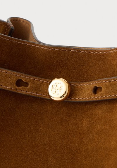 Rudi zomšos batai su lygiu paviršiumi, turintys auksinį mygtuko akcentą ir siuvinėtą kraštą. Mygtukas išryškina logotipo dizainą.